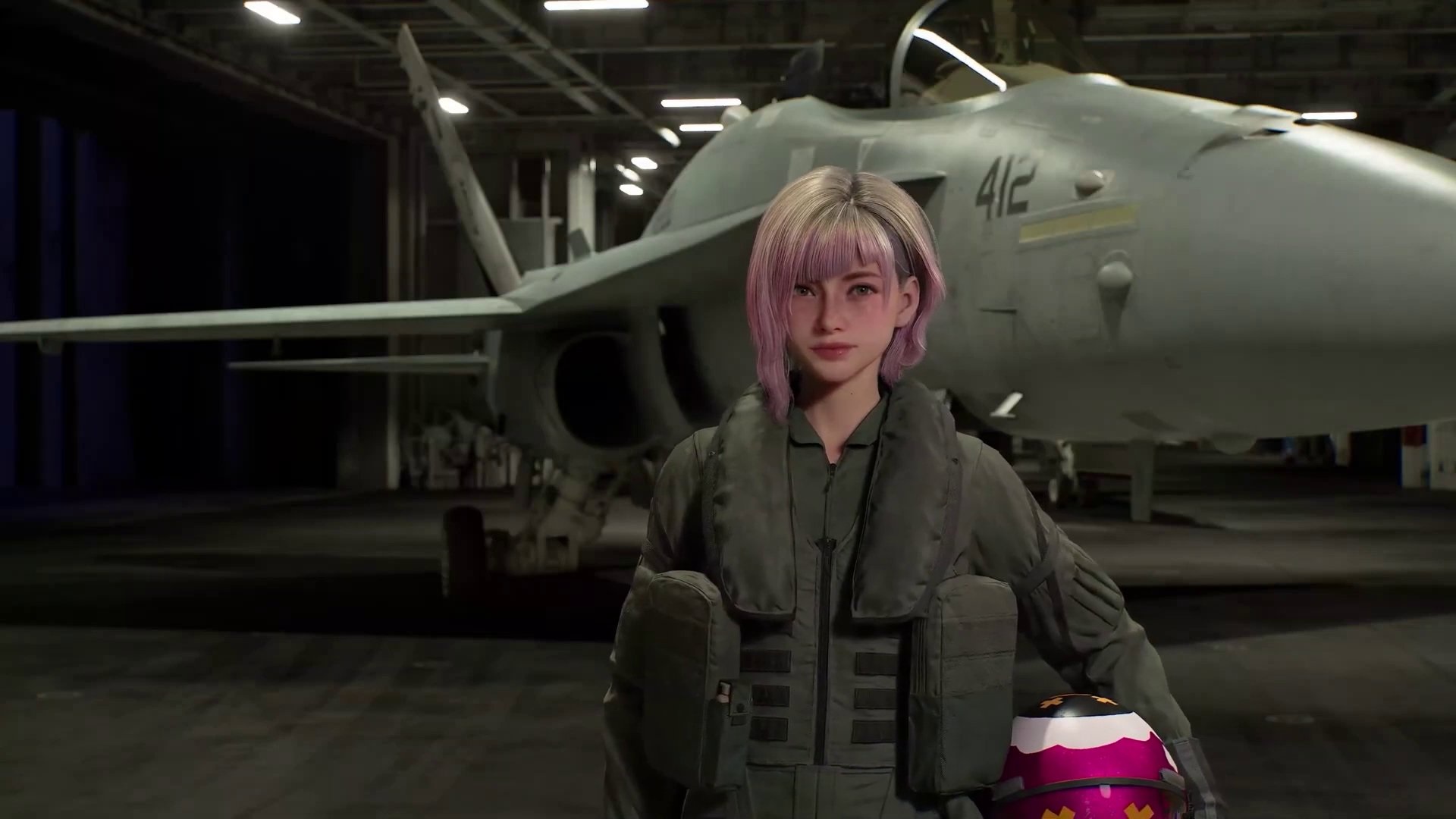 Person in a Green Flight Suit with Pink tinted Hair Stands in a Hangar Beside a Gray Fighter Jet Marked 412 Holding a Pink Helmet in Front