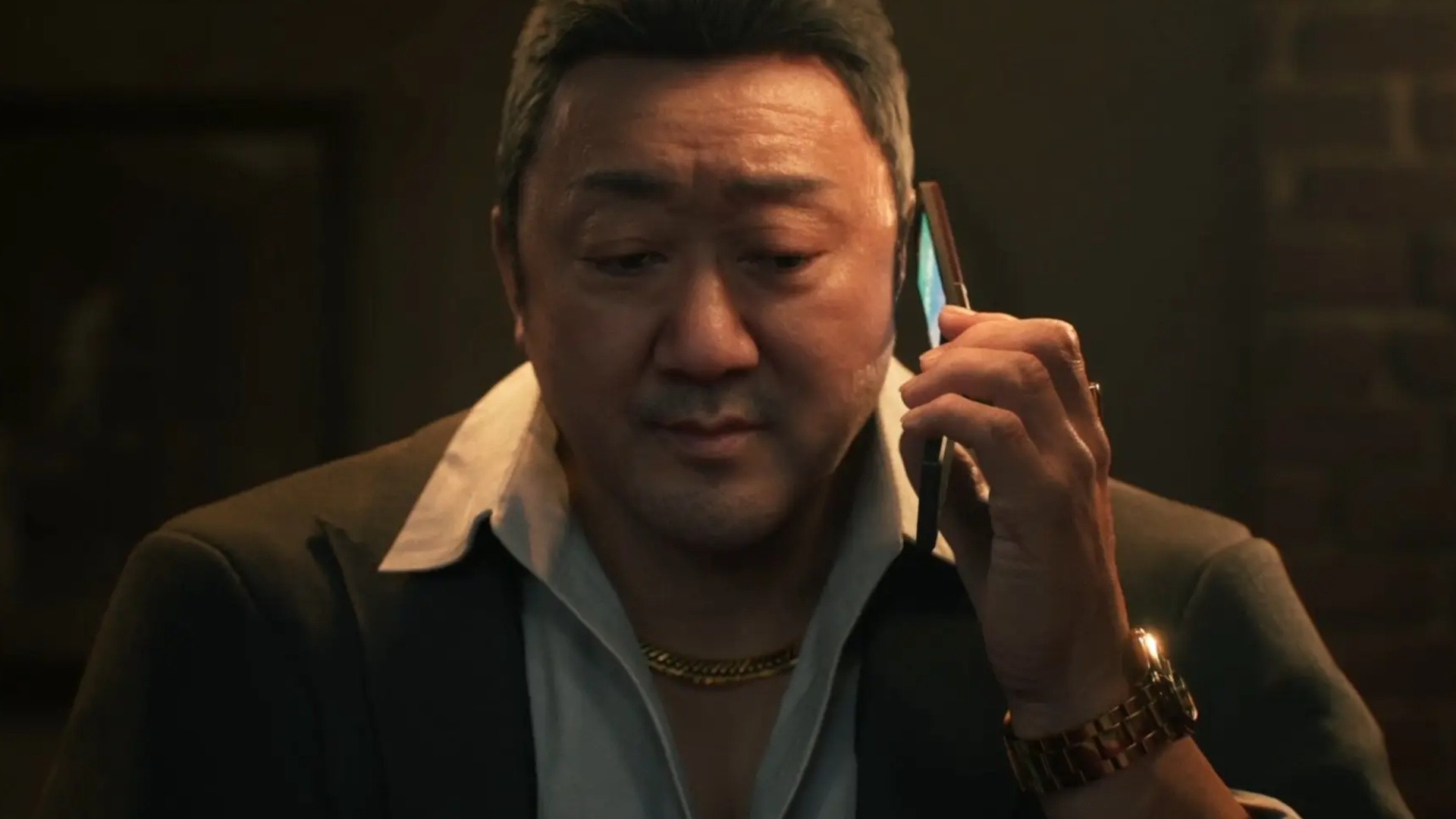 Man in a Suit Talking on a Smartphone in a Dimly Lit Room with a Gold Chain and Watch Visible