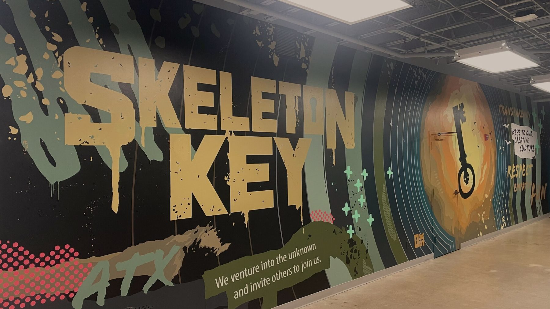 Colorful Mural Along a Hallway Wall with Large Yellow Text Reading 'skeleton Key' and a Unicycle Graphic Amid Circular Blue Spirals
