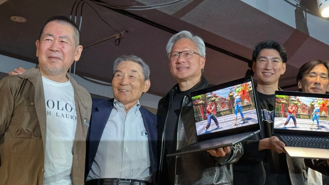 Group of Men Posing Together Two of Them Holding Laptops Showing a Fighting Game on the Screens