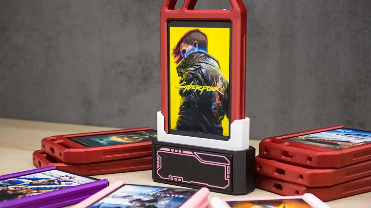 Red Plastic Flip top Game Cartridge Case Standing Upright with a Cyberpunk Poster on a Yellow Background in the Center Several Red and Colored Game Cartridges Lie Flat Around It on a Table